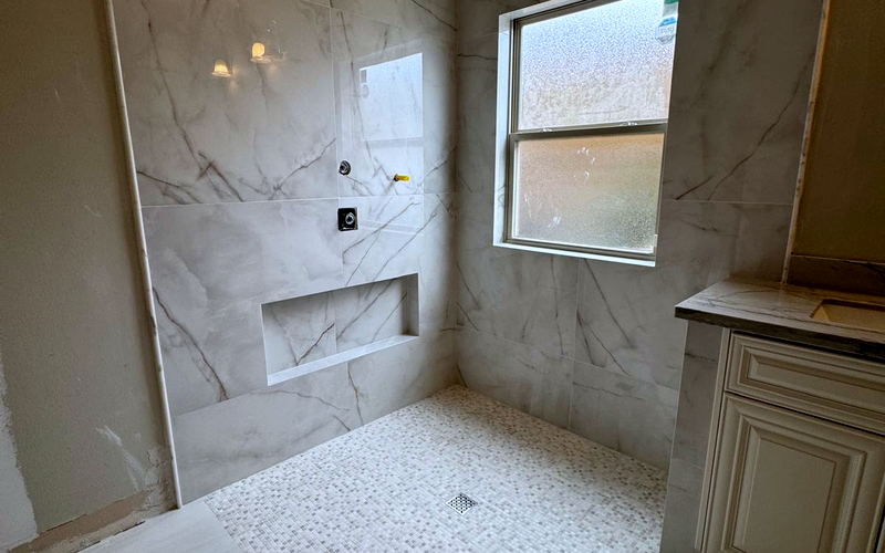 Wide view of a Calacatta-look porcelain shower and bathroom with a mosaic pan and matching large-format floor