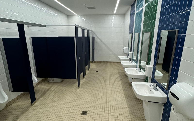 Wide view of a commercial restroom with blue and green tile bands, navy partitions and a tiled floor